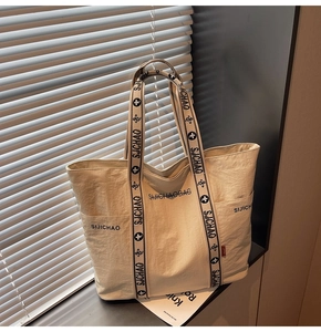 Detail der minimalistischen beigen Canvas-Tasche mit gemustertem Gurt und Seitentasche