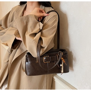 Detail of retro dark brown handbag with buckle and beaded charm worn with a trench coat