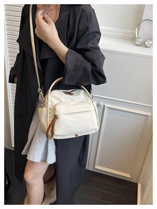 Detail of ivory canvas shoulder bag with brown trim and zipper pockets shown on a model