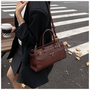 Detailed view of brown leather handbag featuring triangular metal logo on zebra crossing
