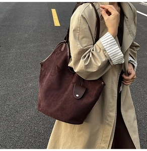 Close-up of a large dark brown suede tote bag featuring a leather flap and metal buckle