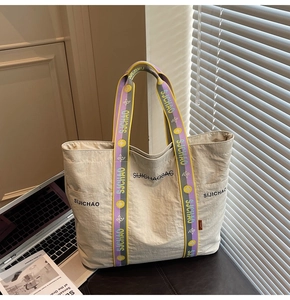 Detail der cremefarbenen Nylon-Tote-Bag mit buntem Streifenschultergurt und Logo