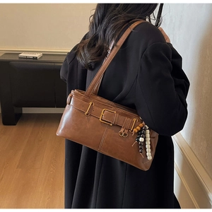 Close-up of brown vintage shoulder bag with buckle strap and beaded charm detail