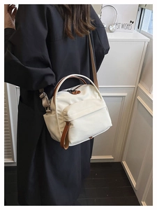 Side view of a beige nylon crossbody bag with brown leather handles worn by a model
