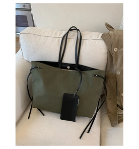 Detail of olive green canvas tote bag with black handles and small hanging pouch on a sofa