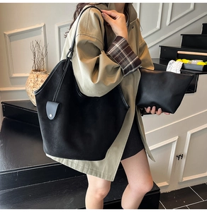 Close-up of black suede tote bag and matching clutch set shown on a female model