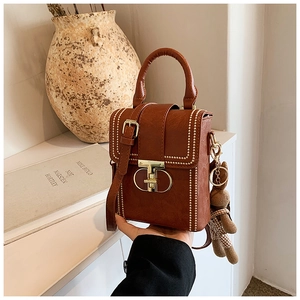 Detailed view of a brown vintage leather square handbag with golden beads and a bear charm