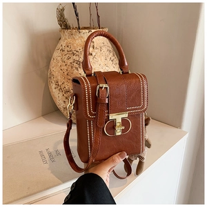 Close-up of brown leather handbag with gold studs, T-lock, and a teddy bear charm
