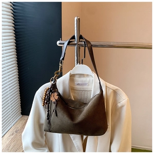 Detail of dark brown suede hobo bag with four-leaf clover charm on white suit