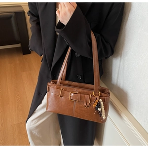 Close-up of brown vintage shoulder bag with metal belt buckle and beaded pendant detail