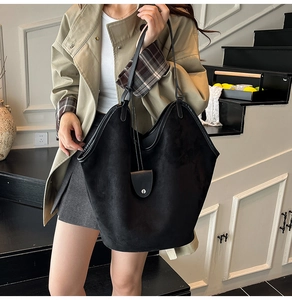 Detail of large black suede tote bag with minimalist shoulder straps on a fashion model