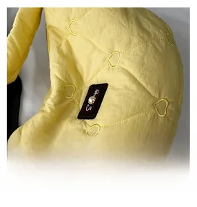 Detail of heart-quilted nylon fabric with pearl-embellished logo patch on yellow bag