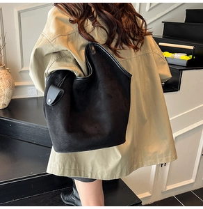 Detail of a black suede tote bag showing large capacity and minimalist leather trim accents