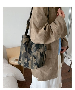 Chic camouflage canvas tote bag with wide strap worn by a model in a minimalist bedroom setting