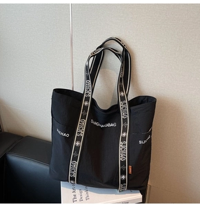 Detail der schwarzen Nylon-Tragetasche mit weißem Logo und Seitentasche auf Buchhintergrund