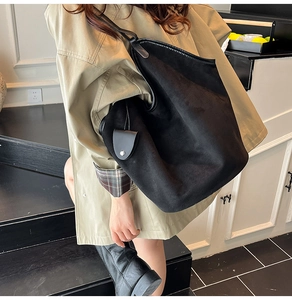 Large black suede tote bag with small pouch worn by a model in a minimalist setting