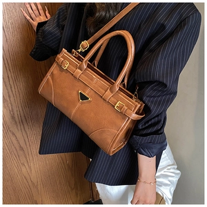 Detailed view of a brown vintage tote bag featuring a black triangular metal plaque