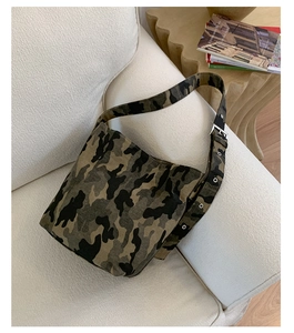 Detail of camouflage canvas shoulder bag with wide strap and metal eyelets on sofa
