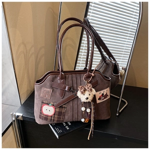 Detail of dark brown tote bag with apple embroidery and plush dog charm on wooden desk