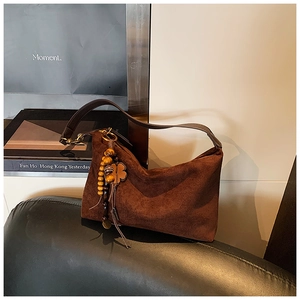 Detail of vintage suede shoulder bag with wooden bead charm and four-leaf clover pendant