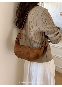 Detailed side view of a brown suede croissant bag on a model in a minimalist setting