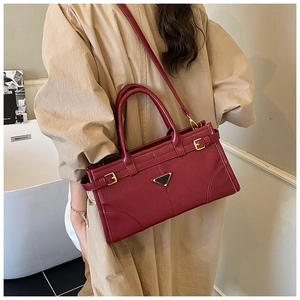 Detail shot of the burgundy leather tote with a metal triangular plaque and buckled straps