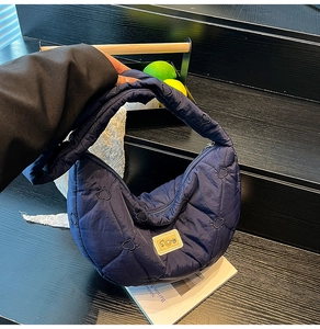 Detail of dark blue heart-stitched puffy dumpling bag with Sunny brand label on wood