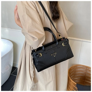 Detail of black glossy handbag featuring gold metal buckles and triangular logo plaque