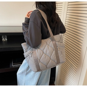 Detailed view of grey quilted tote bag with side zipper and padded texture on model