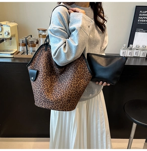 Detail of leopard print tote bag and black clutch held by a model in a cozy cafe