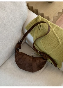 Detail view of brown suede croissant bag on white fabric with adjustable wide strap