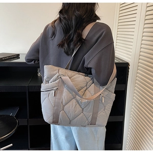 Detail of grey quilted tote bag with diamond stitching and side zippers on model