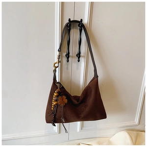 Detail of dark brown suede hobo bag featuring wood bead and clover charm accessory