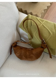 Detailed view of a retro brown suede croissant bag with pleated texture on a soft sofa