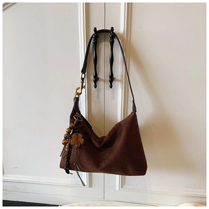 Detail of suede hobo bag with wood bead charm and clover leather patch on white door