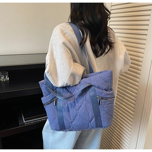 Detail of blue quilted tote bag showing large diamond stitching and wide woven strap