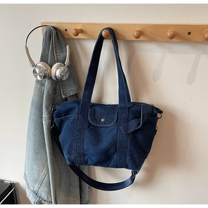 Detail showing deep blue denim tote bag with buckled pocket and adjustable strap