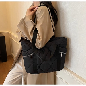 Close-up of black quilted tote bag featuring silver side zippers and woven strap