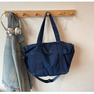 Detail of dark blue denim tote bag featuring front flap pocket and adjustable nylon strap