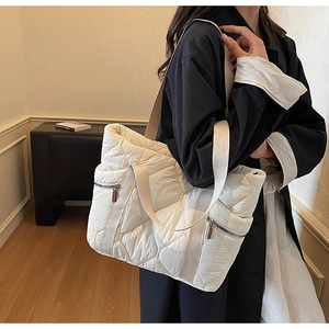 Detailed close-up of a quilted cream tote bag featuring side zipper and webbed straps