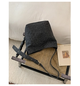 Detail of dark leopard print canvas shoulder bag with adjustable wide strap on a stool