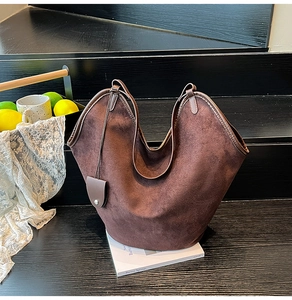 Detailed view of large dark brown suede tote bag with leather straps on a stack of books
