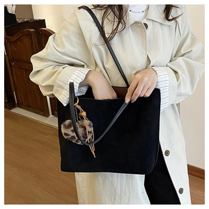 Detail of black suede tote bag featuring a heart-shaped leopard print plush pendant charm