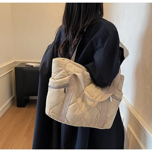 Detailed side view of a beige quilted puffer tote bag worn with a black winter coat