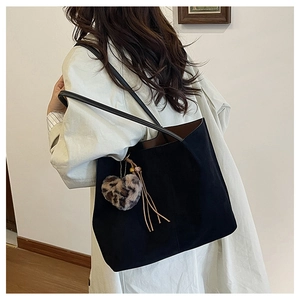 Detail of black matte tote bag with leopard heart charm and tassel on a model