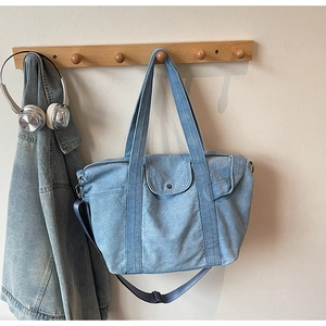 Detail of light blue denim tote bag with adjustable strap and metal snap pocket detail