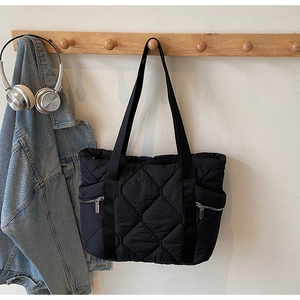 Detail of black quilted tote bag with diamond stitching and side silver zippers on a hanger
