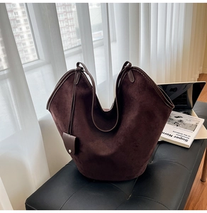 Detail of dark brown suede tote bag with wavy rim and matching charm on leather bench