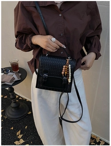 Detail of black woven shoulder bag with beaded charm and silver buckles on model