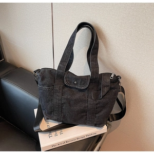 Detail of black washed denim tote bag showing metal zipper and adjustable strap hardware